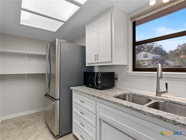 kitchen with stainless steel refrigerator, sink, white cabinets, and light stone counters