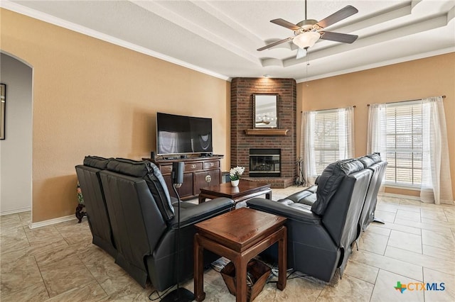 living room featuring crown molding, a tray ceiling, a fireplace, and ceiling fan