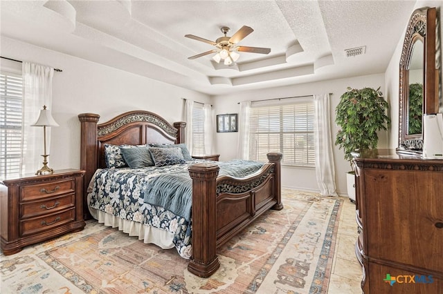 bedroom featuring ceiling fan, a tray ceiling, and a textured ceiling