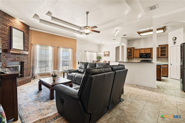 living room featuring ceiling fan, a textured ceiling, a fireplace, and a tray ceiling