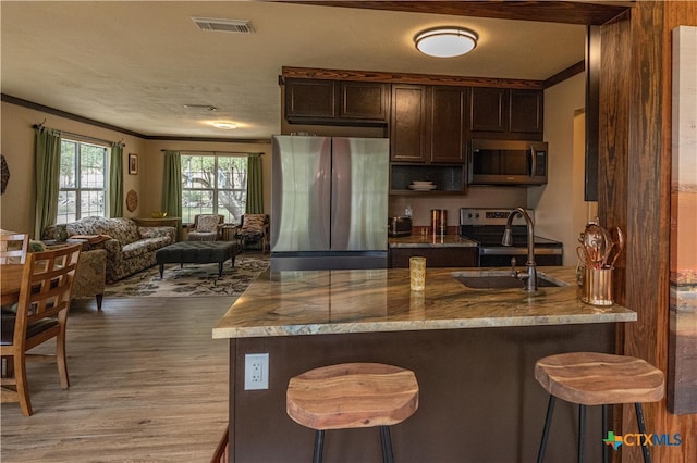 kitchen with light stone counters, stainless steel appliances, light wood-type flooring, dark brown cabinetry, and a breakfast bar