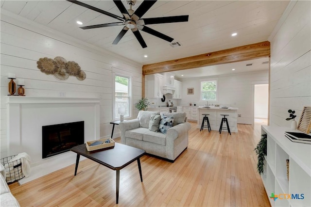 living room with beam ceiling, light wood-type flooring, visible vents, and a healthy amount of sunlight