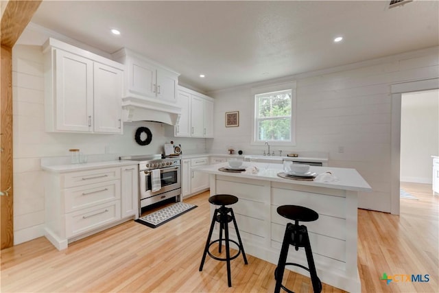 kitchen with light countertops, custom range hood, high end stainless steel range oven, light wood-style flooring, and a kitchen bar