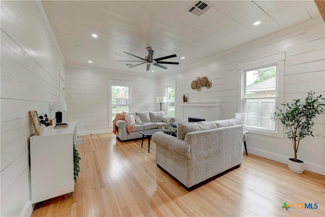 living area with light wood-style floors, plenty of natural light, visible vents, and crown molding