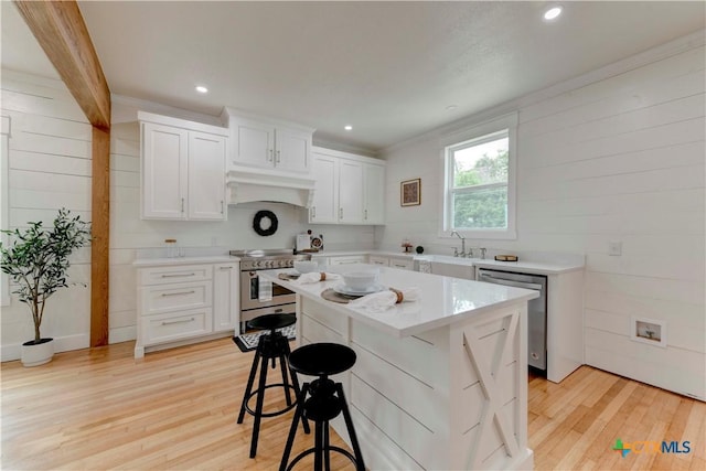 kitchen with light wood-style flooring, a breakfast bar, light countertops, appliances with stainless steel finishes, and range hood