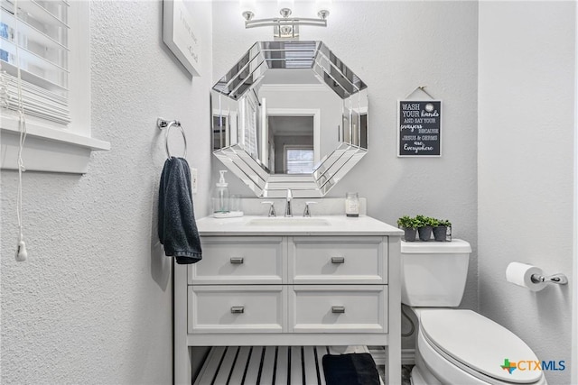 bathroom with toilet, vanity, and a textured wall