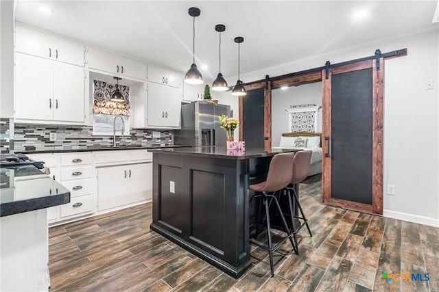 kitchen featuring dark wood finished floors, dark countertops, a barn door, a sink, and stainless steel fridge with ice dispenser