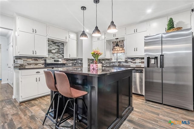 kitchen with dark countertops, dark wood-type flooring, stainless steel appliances, white cabinetry, and backsplash