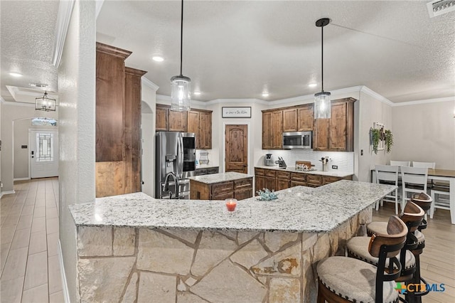 kitchen with a kitchen bar, kitchen peninsula, pendant lighting, and appliances with stainless steel finishes