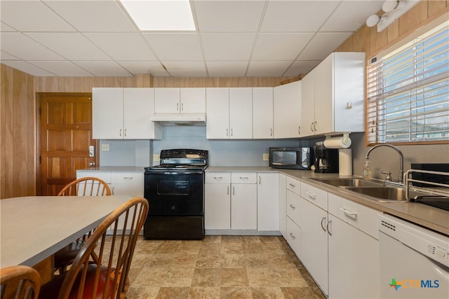 kitchen with wood walls, white cabinetry, sink, black appliances, and a drop ceiling