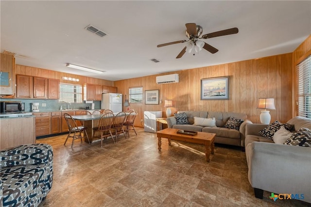 living room featuring ceiling fan, sink, a wall mounted AC, and wooden walls