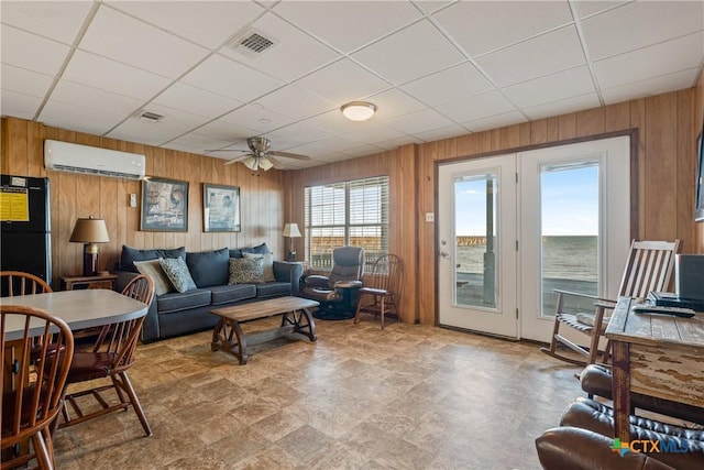 living room with a water view, a drop ceiling, a wall unit AC, and wood walls