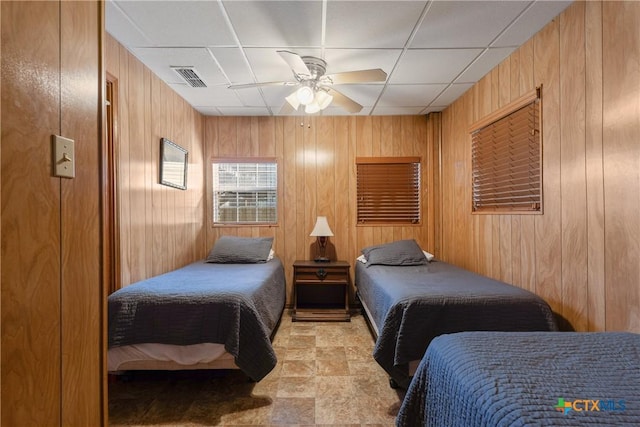 bedroom with wooden walls, ceiling fan, and a paneled ceiling