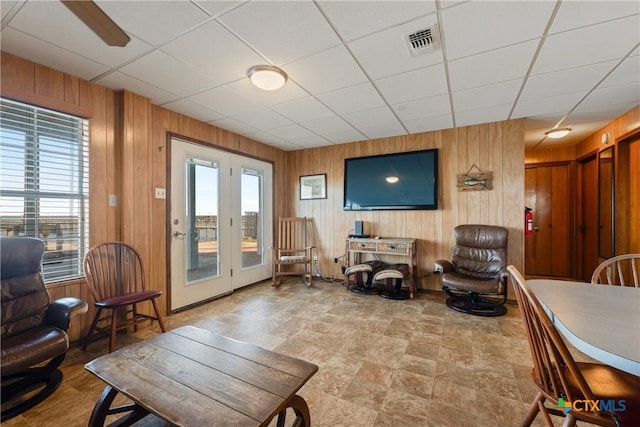 living room with a wealth of natural light, a paneled ceiling, and wood walls