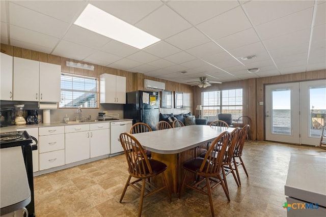 dining space with a paneled ceiling, plenty of natural light, sink, and wood walls