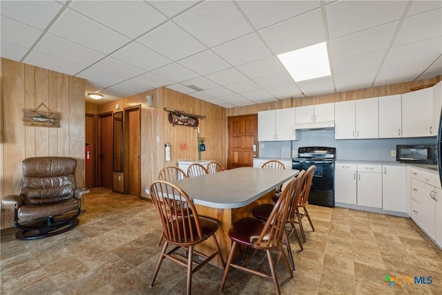 dining area featuring a drop ceiling and wood walls