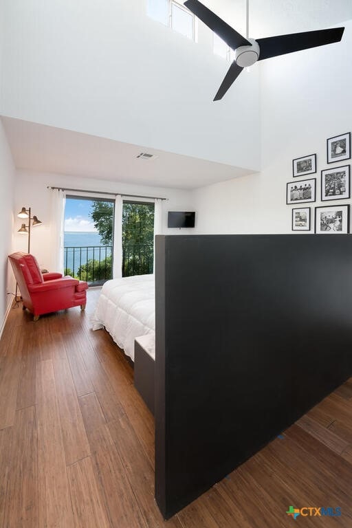 bedroom with access to exterior, visible vents, a towering ceiling, wood finished floors, and a ceiling fan