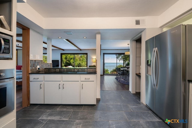 kitchen featuring visible vents, stainless steel appliances, white cabinetry, dark countertops, and backsplash