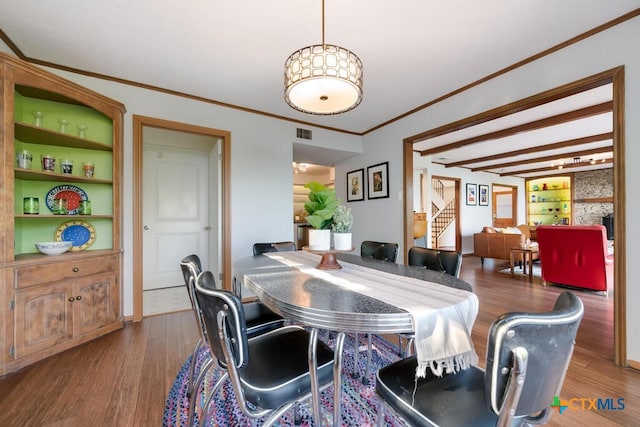 dining space featuring visible vents, built in features, ornamental molding, beam ceiling, and wood finished floors