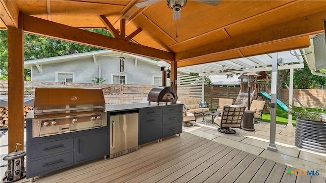 deck with exterior kitchen, a playground, fence, and grilling area