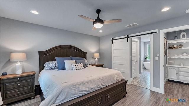 bedroom featuring wood-type flooring, ceiling fan, and a barn door