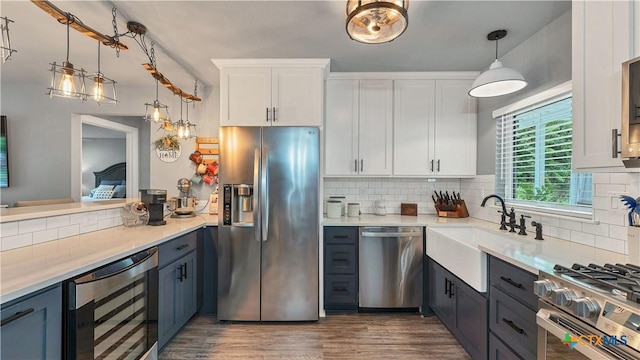 kitchen with backsplash, appliances with stainless steel finishes, white cabinetry, a sink, and beverage cooler