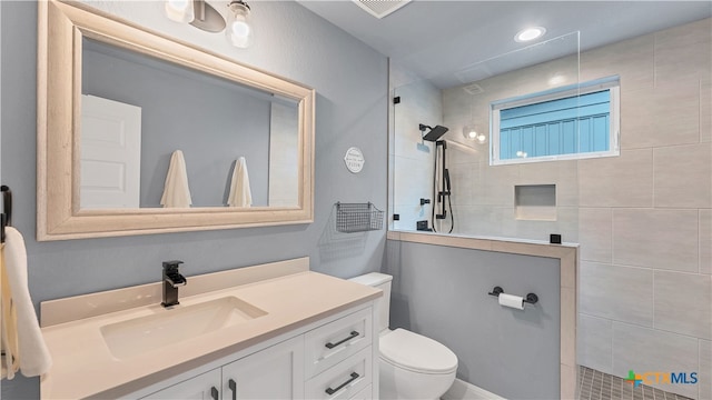 bathroom featuring toilet, a tile shower, and vanity