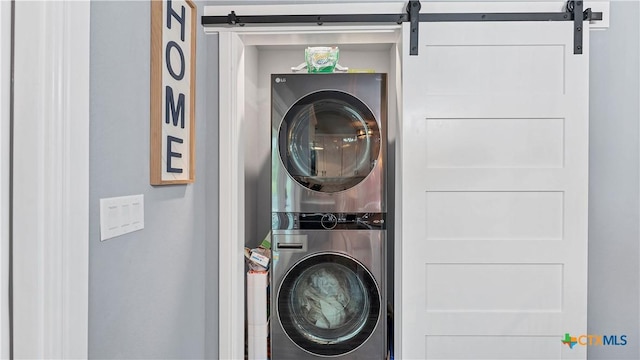 clothes washing area featuring laundry area, a barn door, and stacked washing maching and dryer