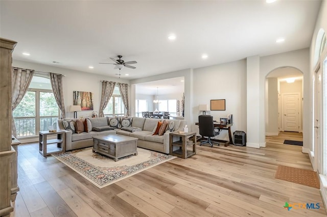 living area featuring arched walkways, recessed lighting, ceiling fan with notable chandelier, baseboards, and light wood finished floors