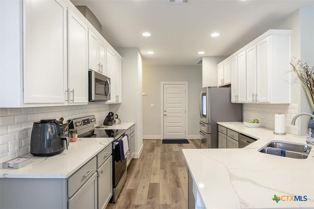 kitchen with light wood finished floors, appliances with stainless steel finishes, white cabinetry, a sink, and light stone countertops