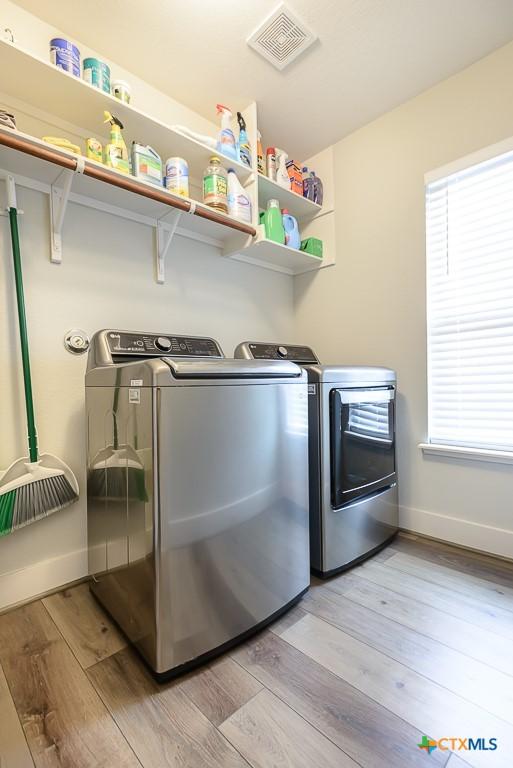 clothes washing area with visible vents, washing machine and dryer, light wood-type flooring, laundry area, and baseboards