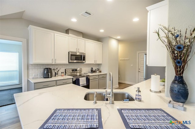 kitchen with visible vents, appliances with stainless steel finishes, white cabinets, a sink, and a peninsula