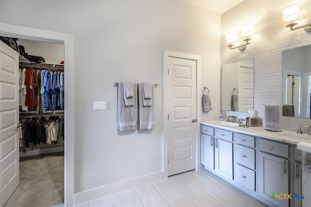 full bath featuring double vanity, a spacious closet, baseboards, and a sink