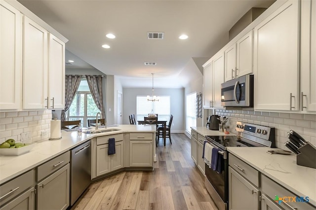 kitchen with visible vents, white cabinets, hanging light fixtures, stainless steel appliances, and a sink