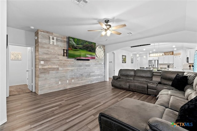 living area featuring arched walkways, ceiling fan, visible vents, and wood finished floors