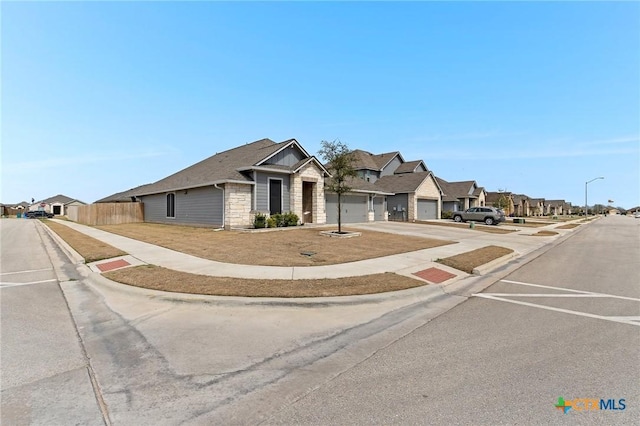 view of front of property featuring stone siding, a residential view, a garage, fence, and concrete driveway