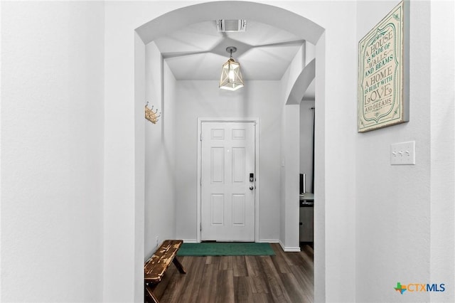 doorway to outside with arched walkways, baseboards, visible vents, and dark wood-type flooring