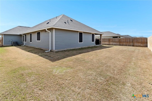 rear view of house with a fenced backyard, a shingled roof, cooling unit, and a lawn