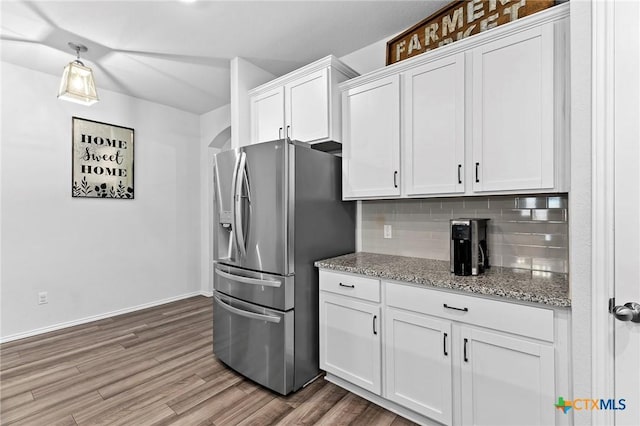 kitchen featuring wood finished floors, stainless steel refrigerator with ice dispenser, white cabinetry, decorative backsplash, and light stone counters
