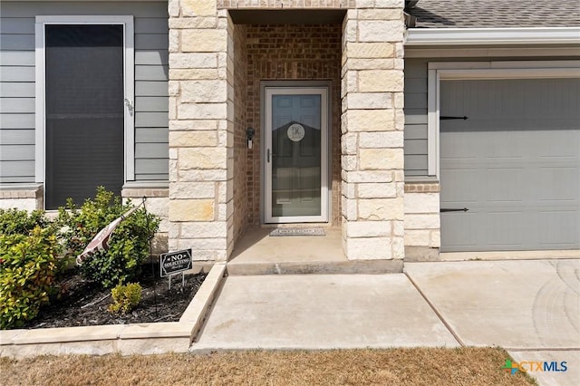 property entrance with stone siding, a shingled roof, and an attached garage