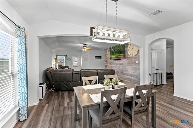 dining space with lofted ceiling, a ceiling fan, visible vents, dark wood-type flooring, and arched walkways