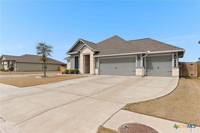 view of front of house featuring fence, a garage, concrete driveway, stone siding, and roof with shingles