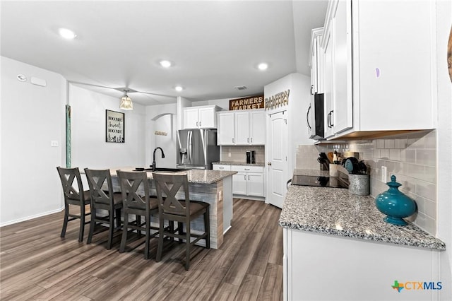 kitchen featuring a breakfast bar area, an island with sink, stainless steel appliances, white cabinetry, and dark wood-type flooring