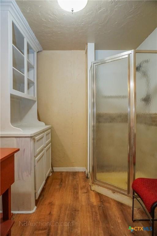 132 Madrona Ln, Bandera, TX 78003 - full bathroom with wood finished floors, a shower stall, a textured ceiling, and baseboards
