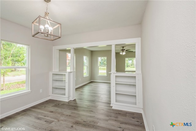 unfurnished dining area with dark wood-type flooring and ceiling fan with notable chandelier