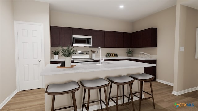 kitchen with light hardwood / wood-style floors, appliances with stainless steel finishes, a center island with sink, and sink