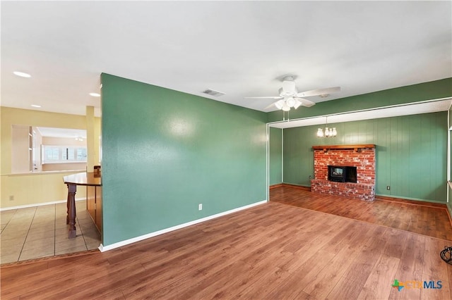 unfurnished living room with a brick fireplace, wood-type flooring, and ceiling fan