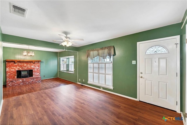 entryway with ceiling fan with notable chandelier, a wood stove, and wood-type flooring