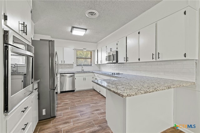 kitchen with stainless steel appliances, white cabinetry, light wood-type flooring, and kitchen peninsula