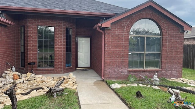 entrance to property featuring fence, a shingled roof, and brick siding